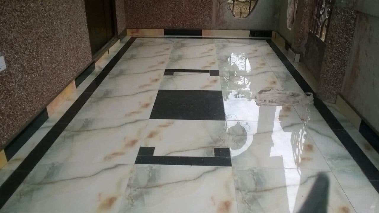 A completed Ibradu interior floor in polished marble-effect tiles with a black inlay border running the length of the hallway