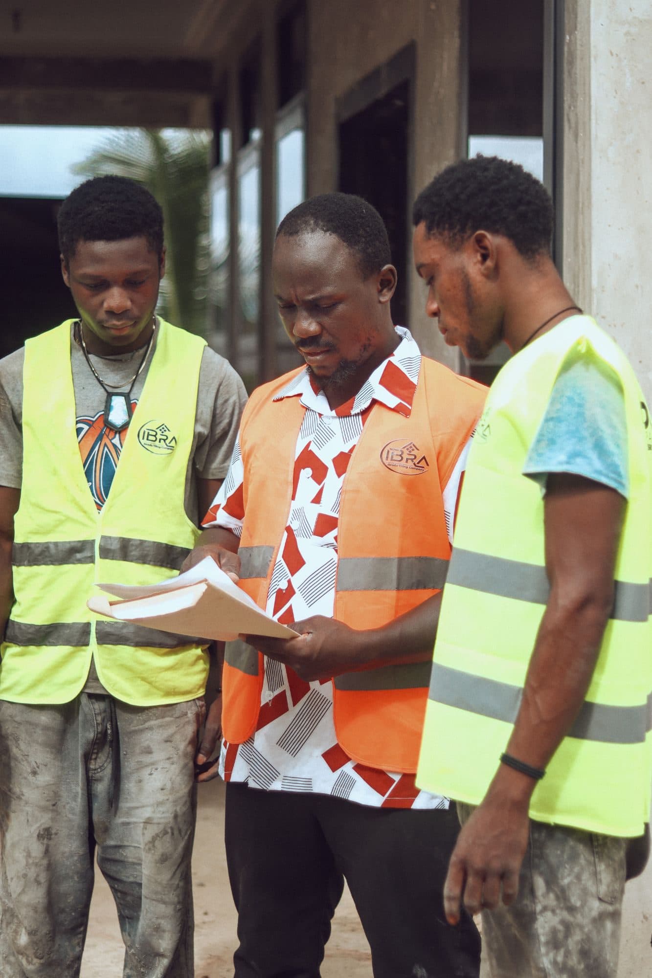 Three members of the Ibradu site team in branded high-visibility vests reviewing project drawings outside a building under construction
